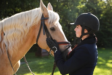 Young woman in horse riding suit and her beautiful pet outdoors on sunny day