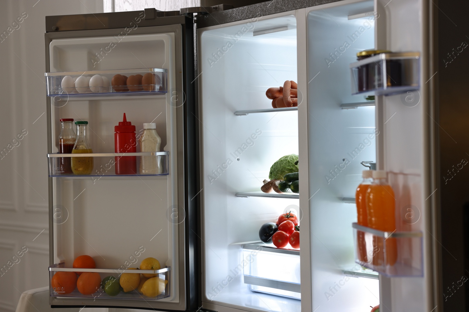 Photo of Open refrigerator full of different products in kitchen