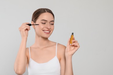 Young woman with eyelash oil on white background, space for text