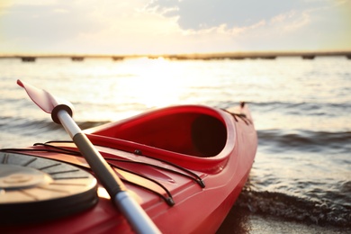 Red kayak with paddle on river at sunset, closeup. Summer camp activity