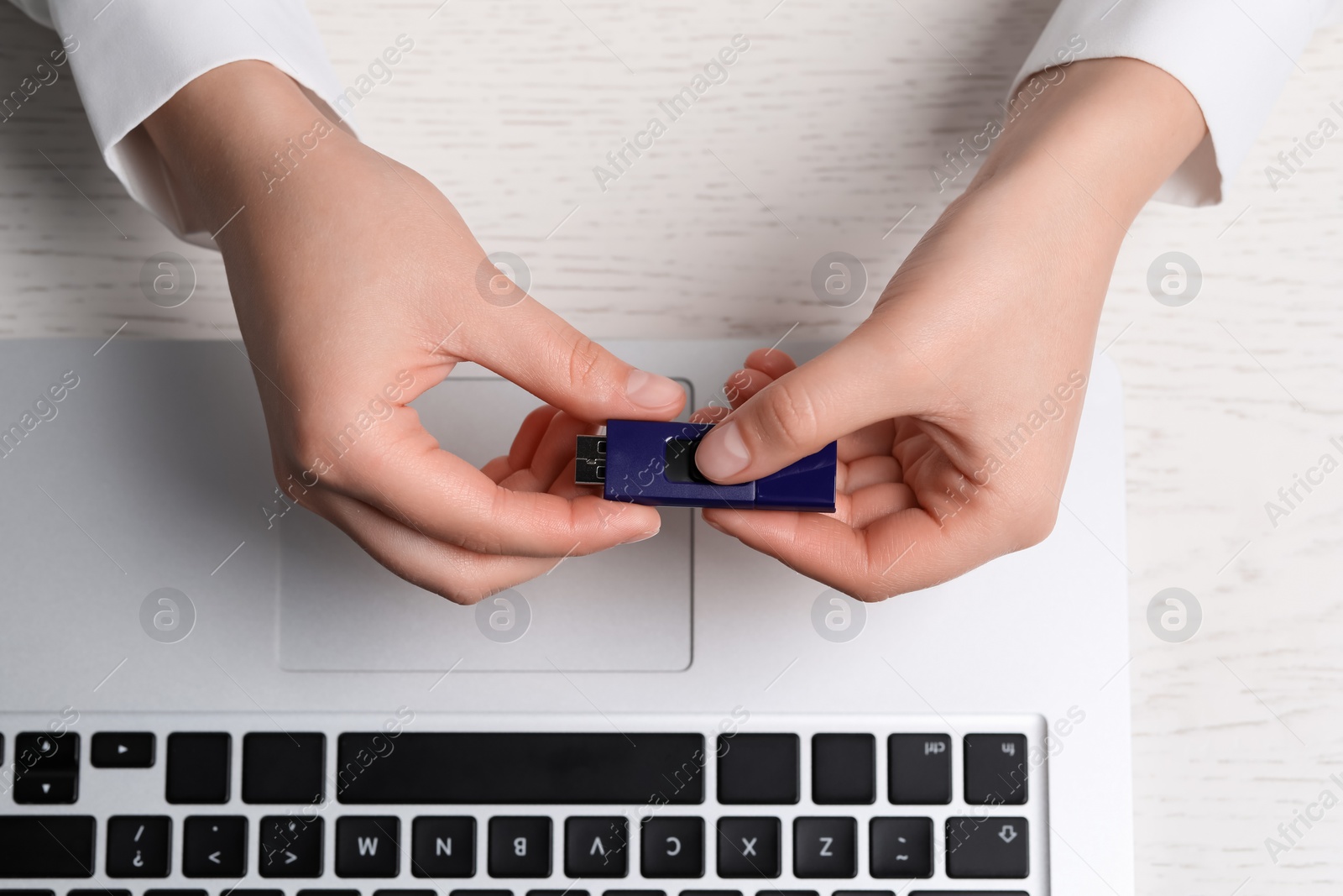 Photo of Woman holding usb flash drive at white wooden table, top view