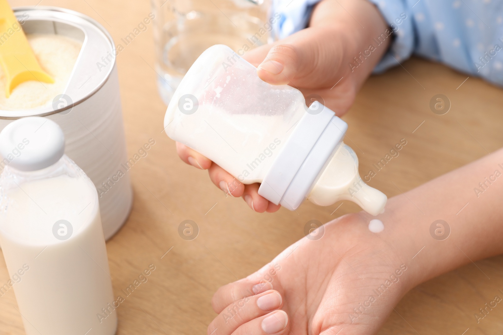 Photo of Woman checking temperature of infant formula at table, closeup. Baby milk