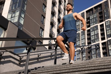 Photo of Happy man running down stairs outdoors on sunny day, low angle view. Space for text