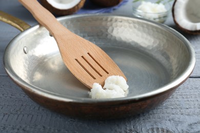 Photo of Frying pan with organic coconut cooking oil and spatula on grey wooden table, closeup