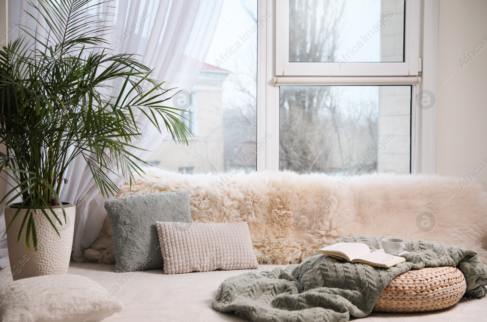 Photo of Comfortable lounge area with faux fur and pillows near window in room