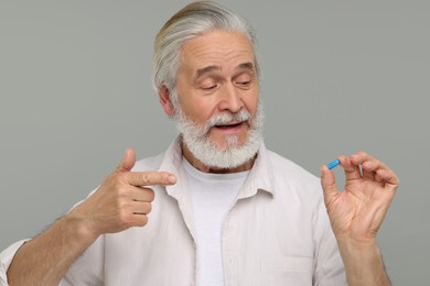 Senior man with pill on grey background