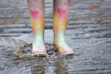 Photo of Woman in rubber boots walking outdoors on rainy day, closeup