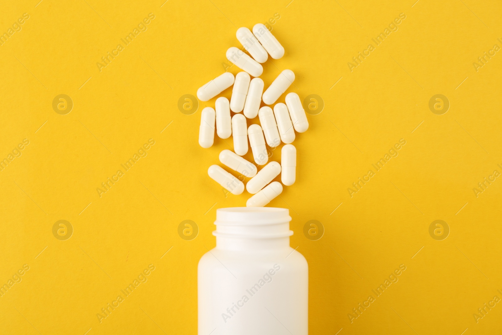 Photo of Bottle and vitamin capsules on yellow background, top view