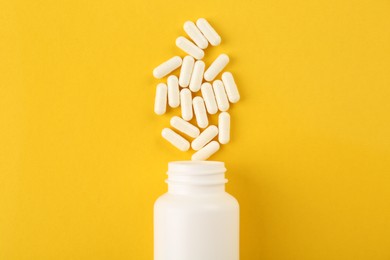 Photo of Bottle and vitamin capsules on yellow background, top view