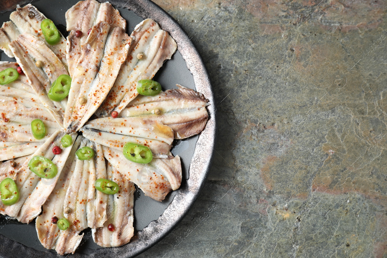 Photo of Tasty pickled anchovies with spices on textured table, top view. Space for text