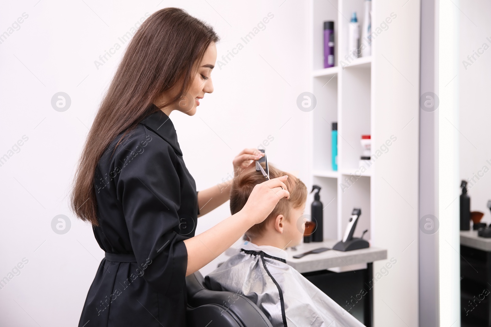 Photo of Professional female hairdresser working with little boy in salon