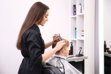 Photo of Professional female hairdresser working with little boy in salon