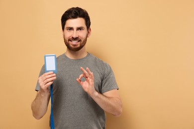 Photo of Happy man with VIP pass badge showing OK gesture on beige background, space for text