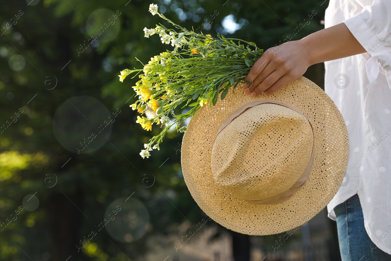 Photo of Young woman with straw hat and bouquet outdoors on sunny day, closeup