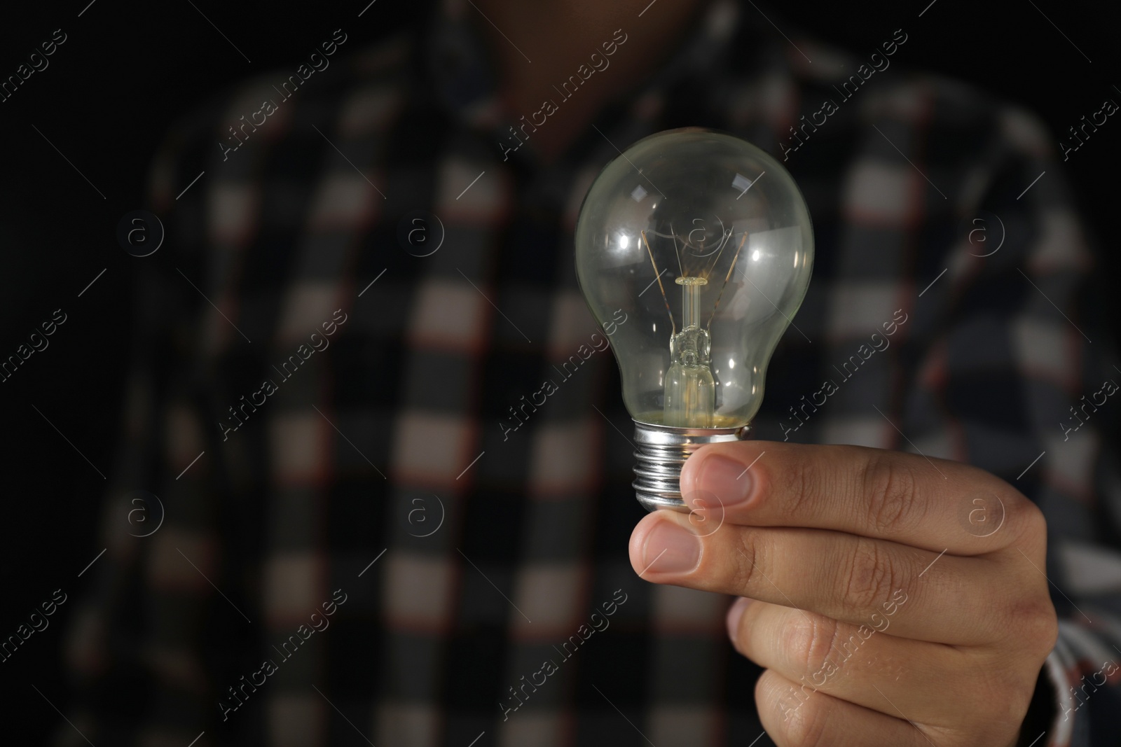 Photo of Man holding incandescent light bulb on dark background, closeup. Space for text