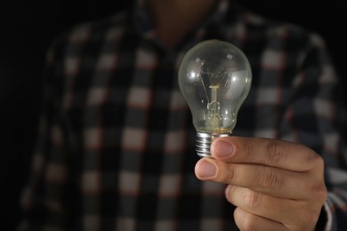 Photo of Man holding incandescent light bulb on dark background, closeup. Space for text