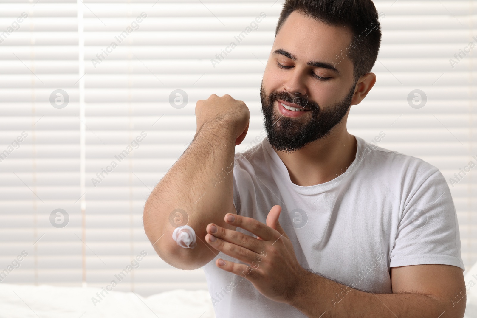 Photo of Man with dry skin applying cream onto his elbow indoors, space for text