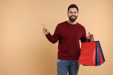 Photo of Smiling man with many paper shopping bags pointing at something on beige background. Space for text