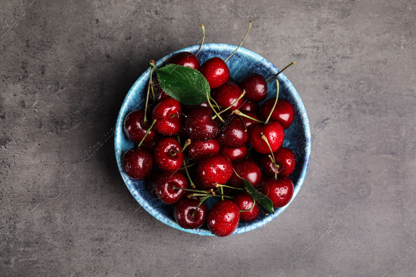 Photo of Bowl with delicious sweet cherries on grey table, top view