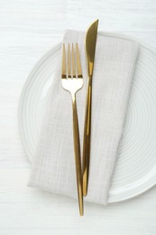 Stylish ceramic plate, cutlery and napkin on white wooden table, top view