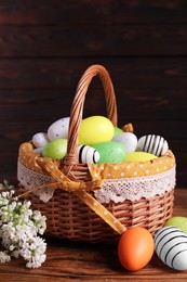 Photo of Wicker basket with festively decorated Easter eggs and white lilac flowers on wooden table