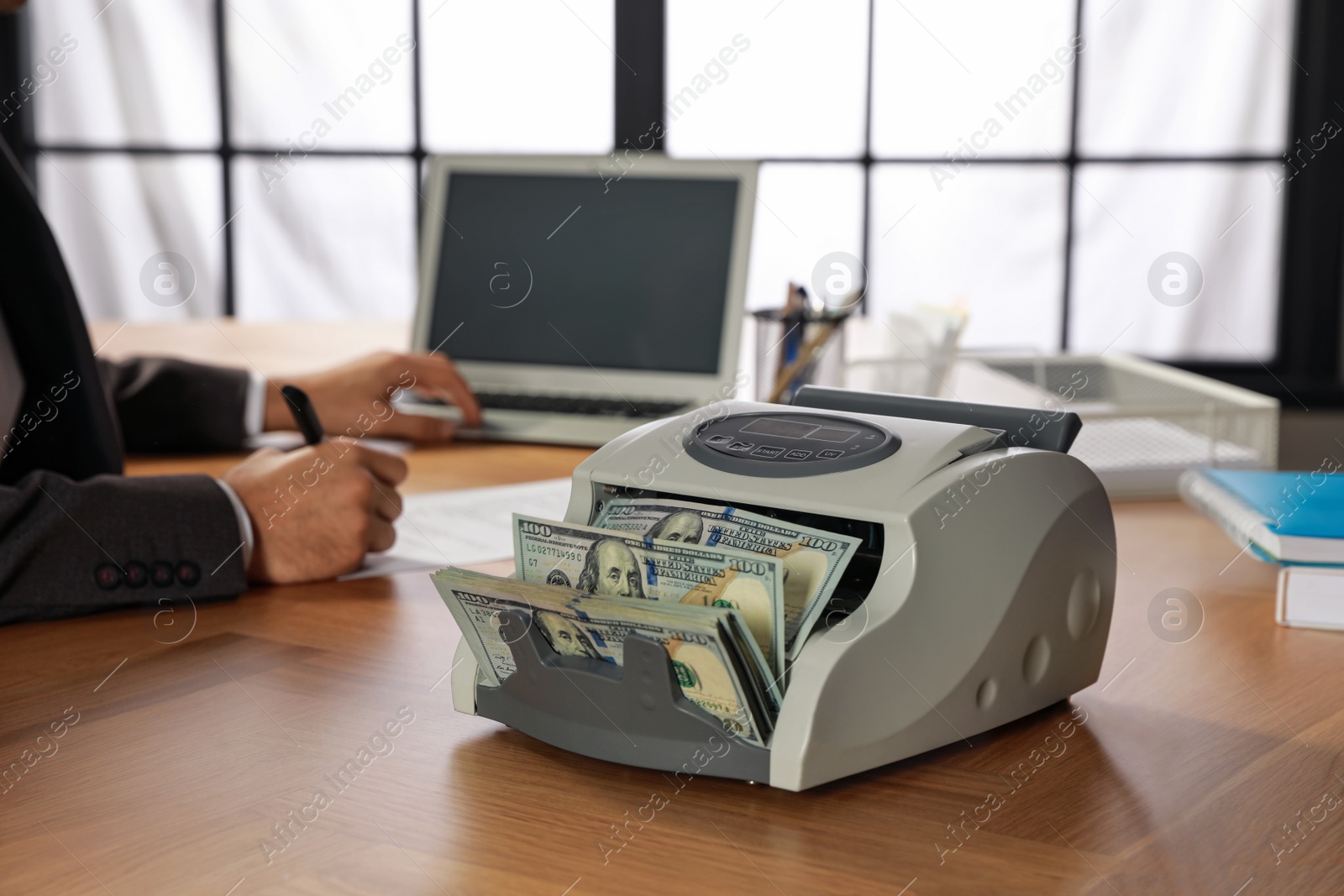 Photo of Modern banknote counter with money and man working at wooden table indoors, closeup
