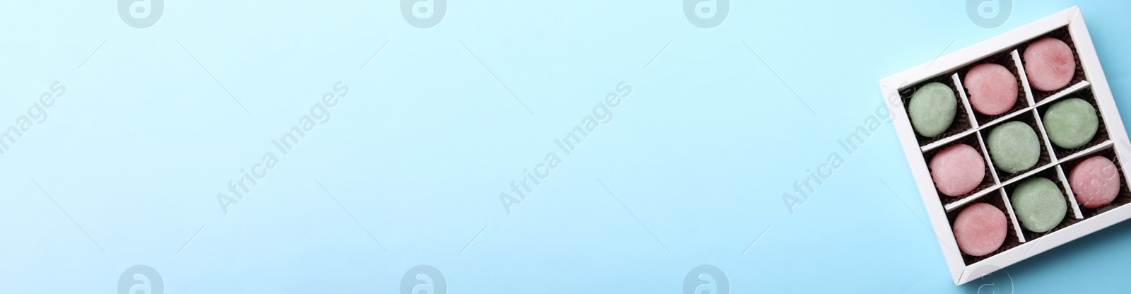 Photo of Many different delicious mochi in box on light blue background, top view with space for text. Traditional Japanese dessert