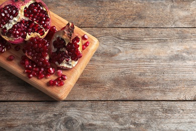 Board with ripe pomegranates and seeds on wooden background, top view. Space for text