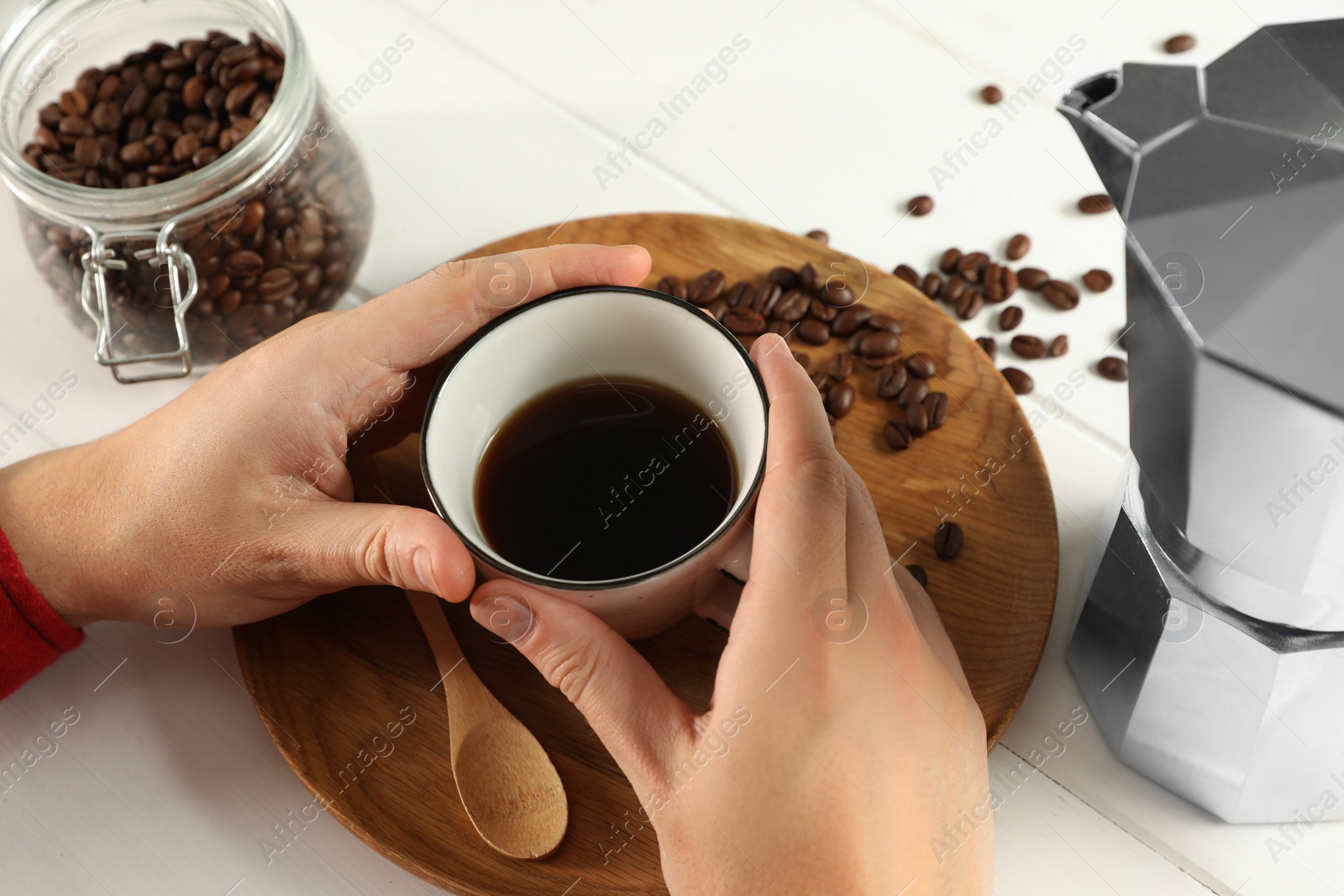 Photo of Man with cup of aromatic brewed coffee, closeup. Moka pot and beans on white wooden table