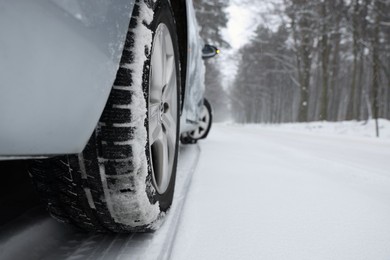 Car with winter tires on snowy road in forest, closeup. Space for text