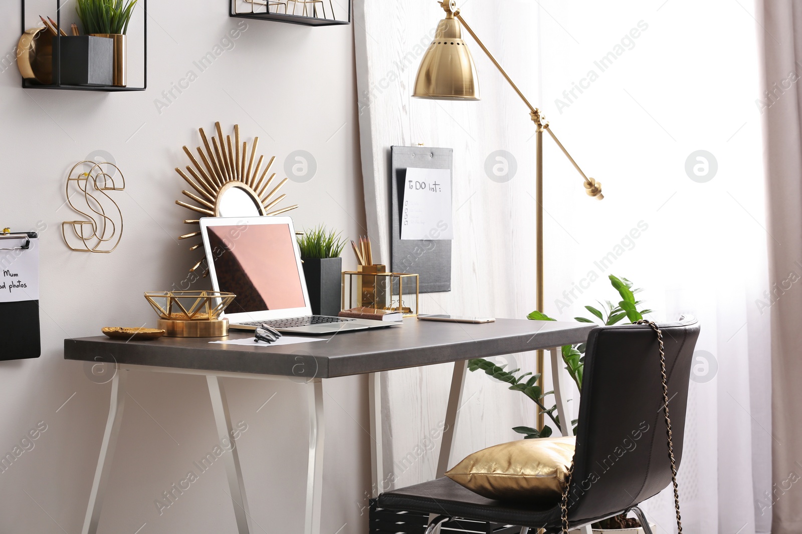 Photo of Modern workplace with laptop and golden decor on desk near wall. Stylish interior design