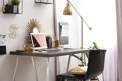 Photo of Modern workplace with laptop and golden decor on desk near wall. Stylish interior design