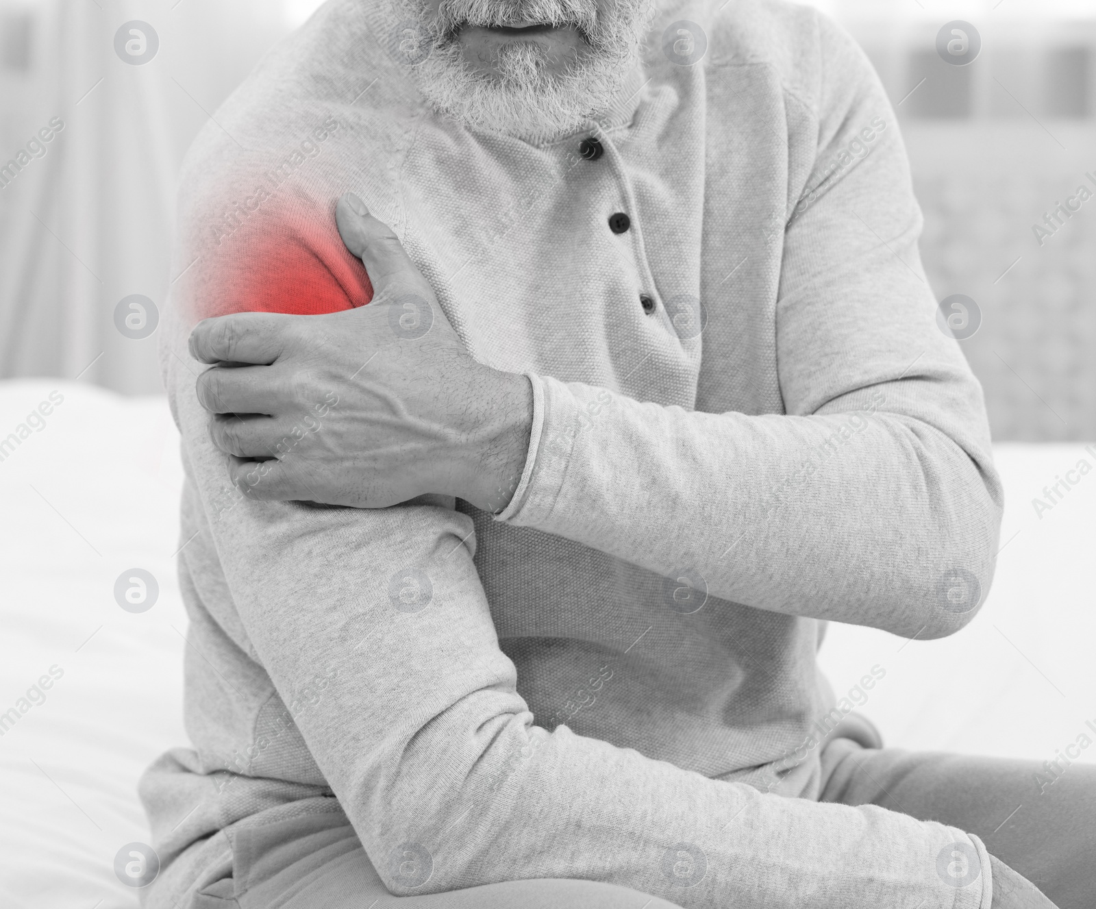 Image of Man suffering from pain in shoulder on bed at home, closeup. Black and white effect