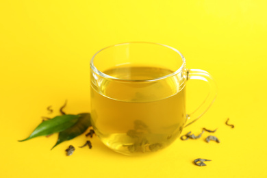 Photo of Cup of green tea and leaves on yellow background