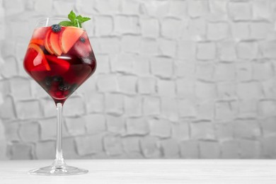 Photo of Glass of Red Sangria with fruits on white wooden table, space for text