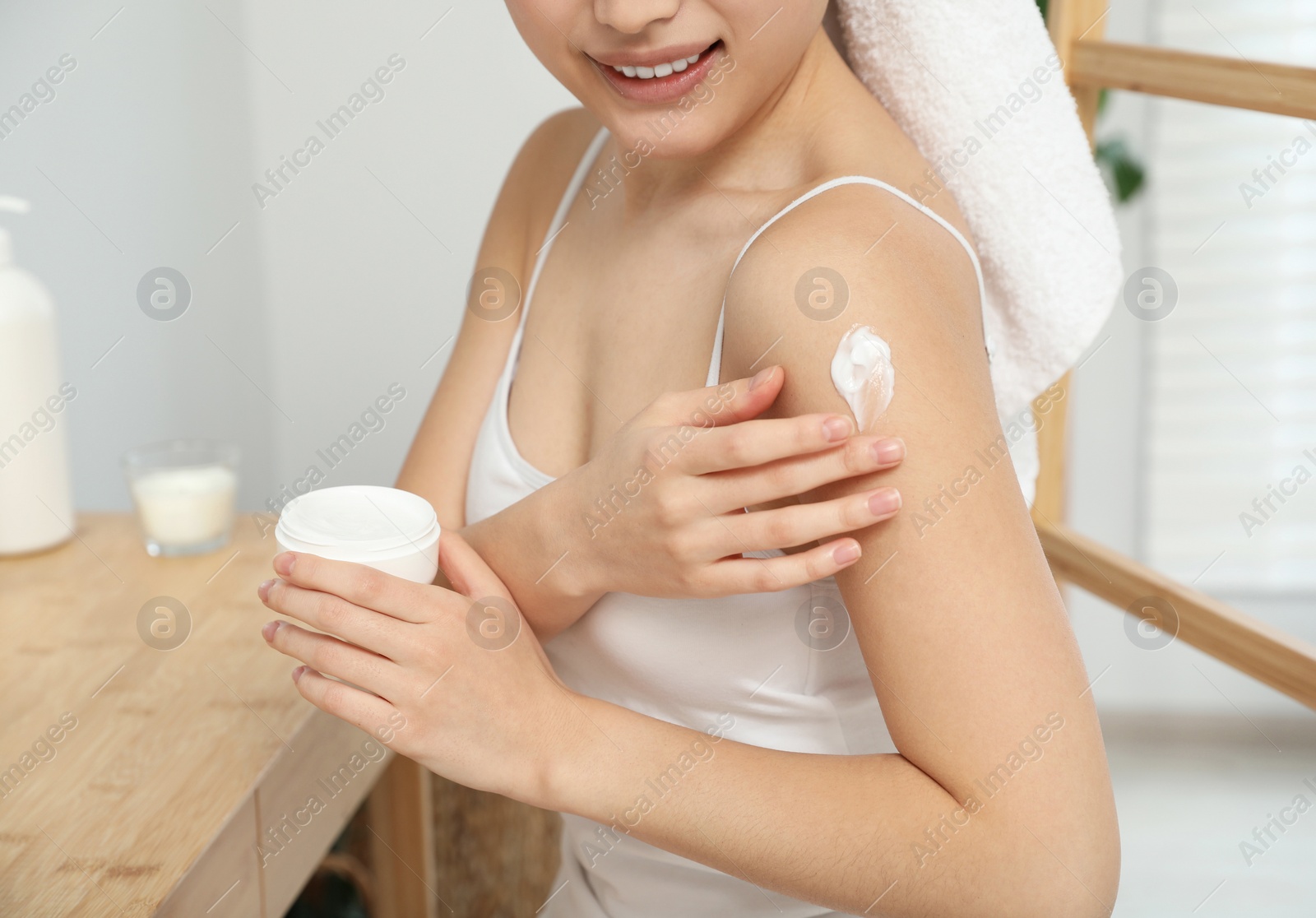 Photo of Young woman applying body cream on shoulder indoors, closeup