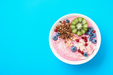 Photo of Tasty smoothie bowl with fresh kiwi fruit, berries and granola on light blue background, top view. Space for text