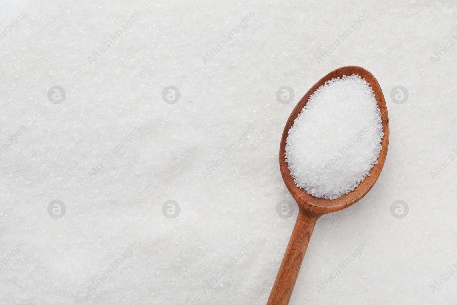 Photo of Wooden spoon on granulated sugar, top view. Space for text