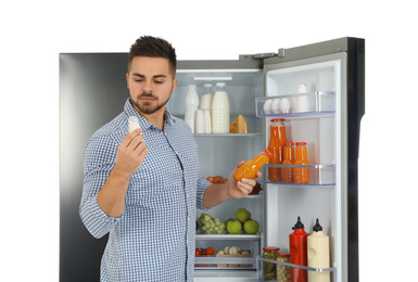 Young man choosing food from refrigerator on white background