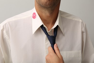 Photo of Woman grabbing her husband by tie due lipstick kiss mark on his shirt, closeup