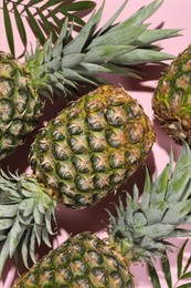 Photo of Whole ripe pineapples and green leaves on pale pink background, flat lay