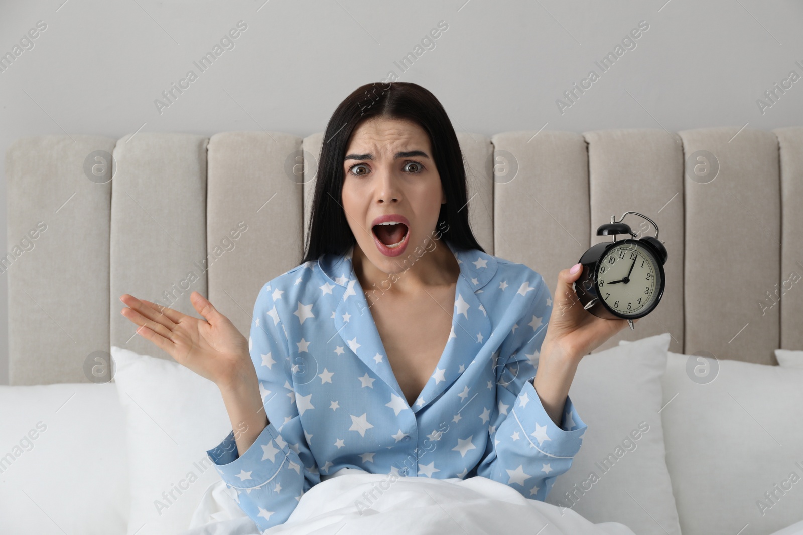 Photo of Emotional overslept woman with alarm clock in bed. Being late concept