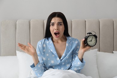 Photo of Emotional overslept woman with alarm clock in bed. Being late concept