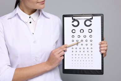 Photo of Ophthalmologist pointing at vision test chart on gray background, closeup