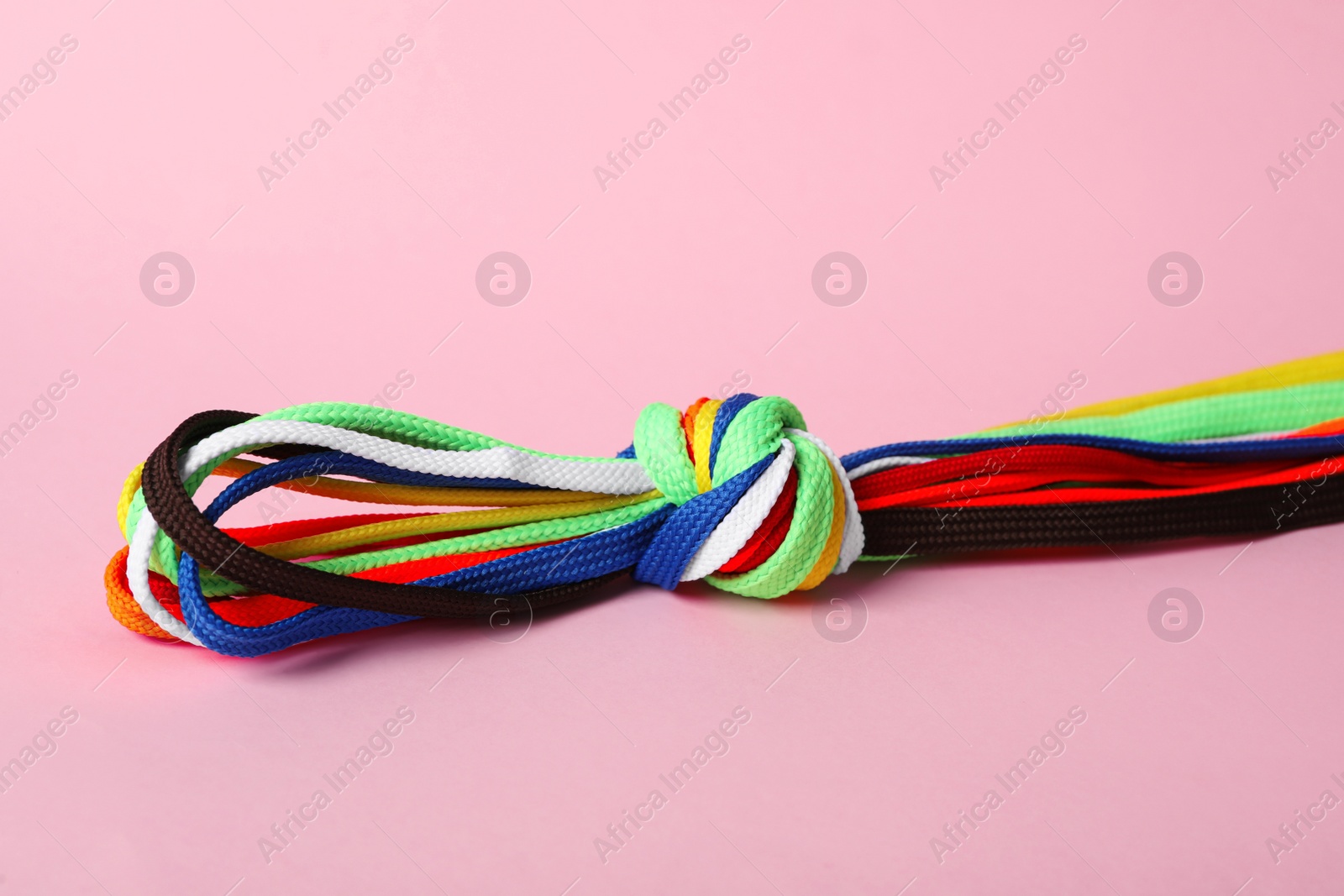 Photo of Many colorful shoe laces tied in knot on light pink background