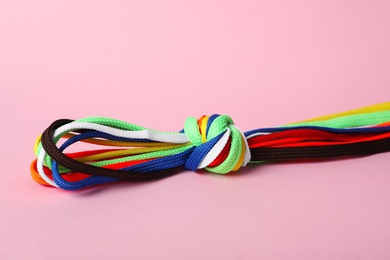 Photo of Many colorful shoe laces tied in knot on light pink background