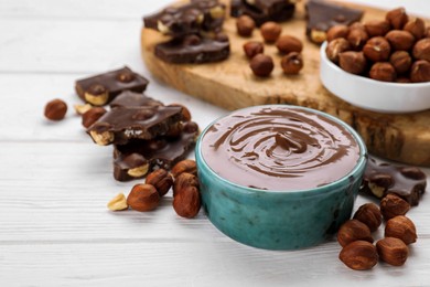 Bowl with tasty paste, chocolate pieces and nuts on white wooden table