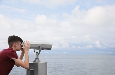 Photo of Teenage boy looking through mounted binoculars near sea. Space for text
