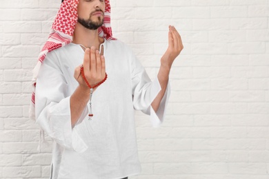 Photo of Muslim man praying near brick wall, closeup