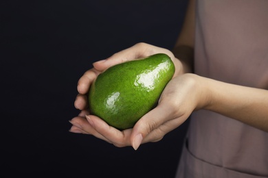 Photo of Woman holding ripe fresh avocado on dark background, closeup